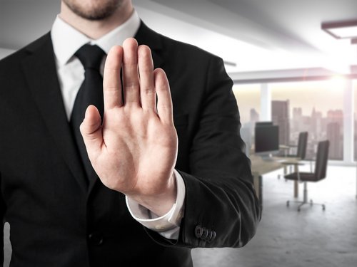 Mann im Anzug im Büro, hält die Hand als Widerspruchsignal nach oben