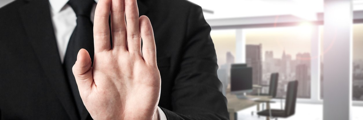 Mann im Anzug im Büro, hält die Hand als Widerspruchsignal nach oben