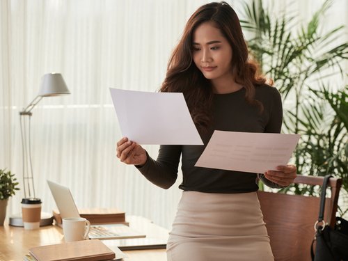 Frau im Arbeitszimmer. In der einen Hand hält sie einen Aufhebungsvertrag und in der anderen Hand eine Kündigung