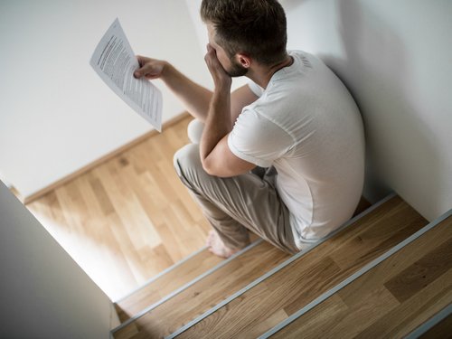 Kranker Mann sitzt auf der Treppe mit Kündigung in der Hand